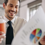 Uśmiechnięty pan w jednej ręce trzymający kubek z kawą a w drugiej wykres przedstawiający ścieżkę kariery w finansach.