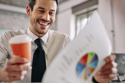 Uśmiechnięty pan w jednej ręce trzymający kubek z kawą a w drugiej wykres przedstawiający ścieżkę kariery w finansach.