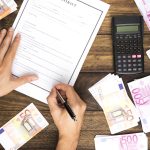 Ręce inwestora podpisujące kontrakt obok kalkulatora i stosów gotówki, co reprezentuje zyskowny portfel, jaki oferują detaliczne fundusze wierzytelności.