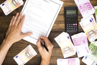 Ręce inwestora podpisujące kontrakt obok kalkulatora i stosów gotówki, co reprezentuje zyskowny portfel, jaki oferują detaliczne fundusze wierzytelności.