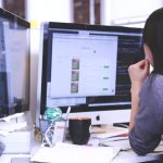 Kobieta pracująca przy biurku z dwoma monitorami wyświetlającymi arkusze danych i kod, pokazująca jak wygląda nowoczesna ścieżka kariery w finansach.