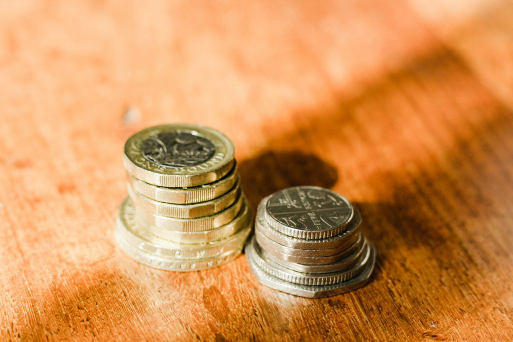 Ułożone w małe stosy monety leżące na drewnianej powierzchni jako symbol oszczędzania i zarządzania finansami.